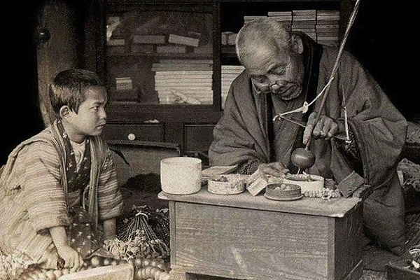 old photograph of elder teaching young boy to make object apprenticeship