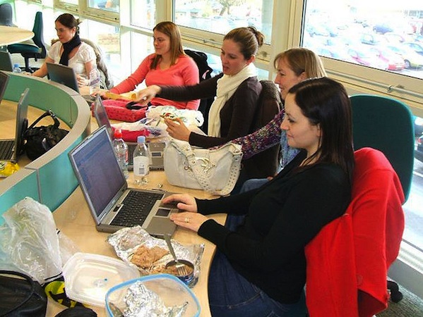 5 women working on laptops around conference table