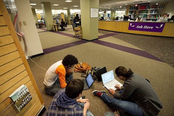 students sitting together in library studying working on computer