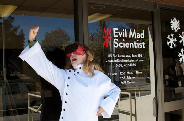 woman in lab coat and virtual reality headset in front of Evil Mad Scientist building
