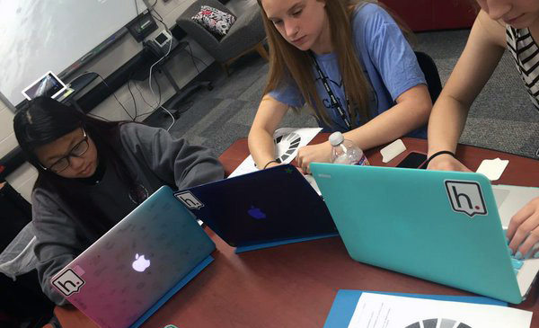 3 young female students sitting at table and looking at their laptop screens