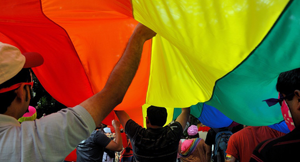 People standing under a large LGBTQ flag