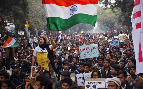 large crowd of protesters holding signs and waving flags in India