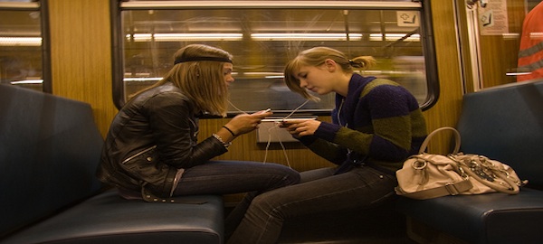 2 students sitting on subway texting listening to music