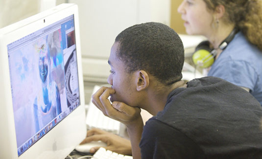 Young African American boy leaning over looking at computer screen