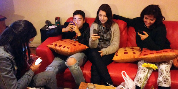 Four teenagers looking at smartphone screens while sitting on couch