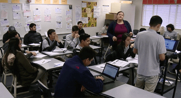 Teacher standing in middle of classroom surrounded by students