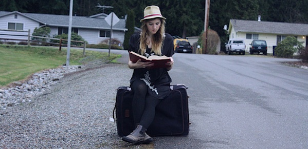 girl sitting on suitcase reading in street